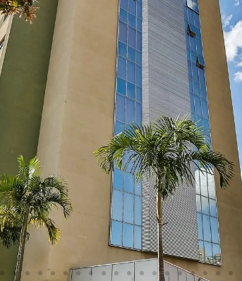 Parte da visão do prédio do Hotel Nobile Inn Pampulha. Há um prédio alto em cor amarelada, parcialmente espelhado com duas palmeiras próximas.
